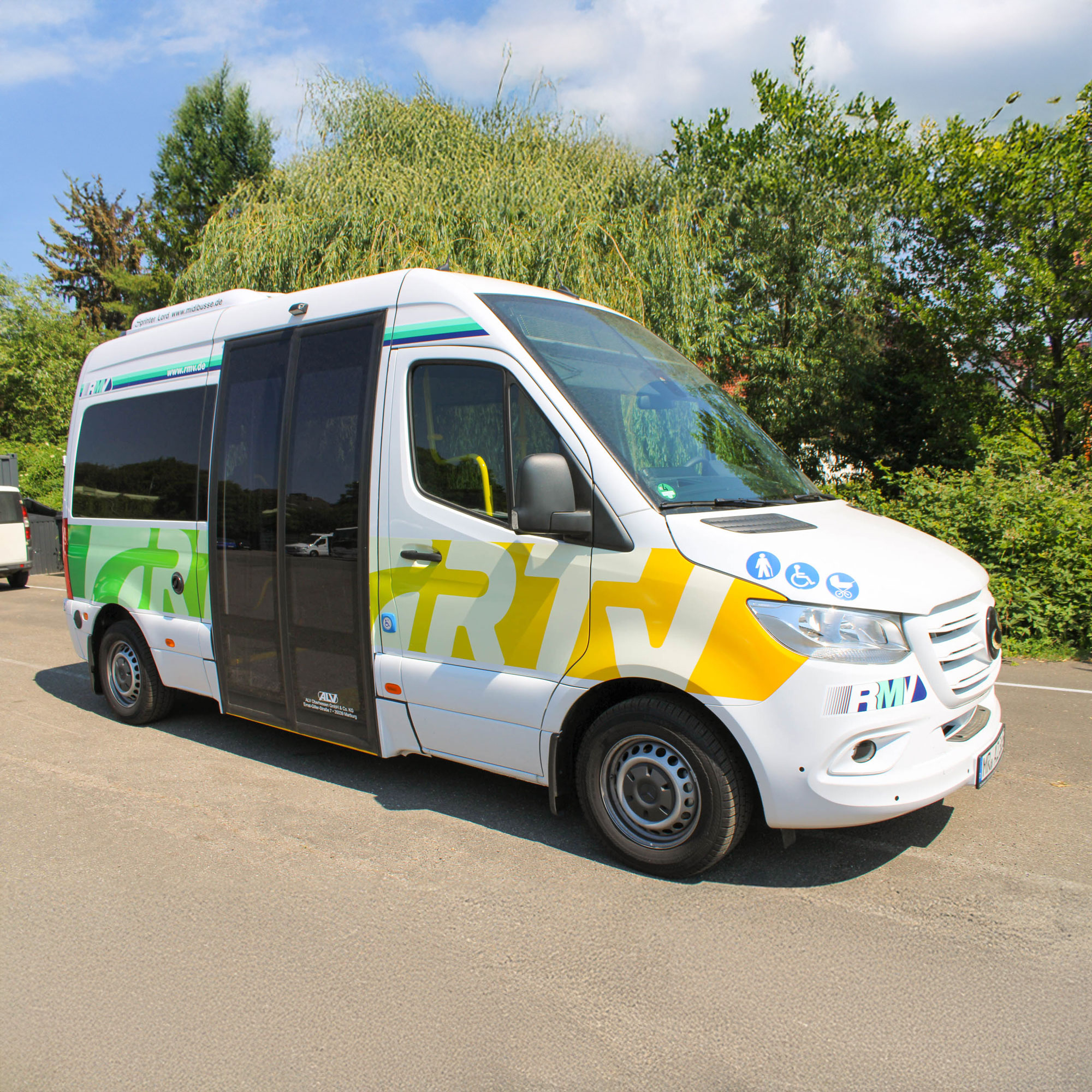 Der Rufbus der Rheingau-Taunus-Verkehrsgesellschaft parkt auf einer Straße, umgeben von Bäumen. Das kompakte Fahrzeug zeigt das RTV-Design in Gelb und Grün und trägt Symbole für Barrierefreiheit.